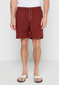 Mann in burgunderfarbenen Z drawstring-Shorts, weißem T-Shirt und weißen Flip-Flops steht vor einem schlichten Hintergrund.