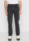 Schwarze Denim-Jeans mit geradem Schnitt, fünf Taschen und einem Metallknopfverschluss. Getragen mit einem weißen T-Shirt und Sneakers.
