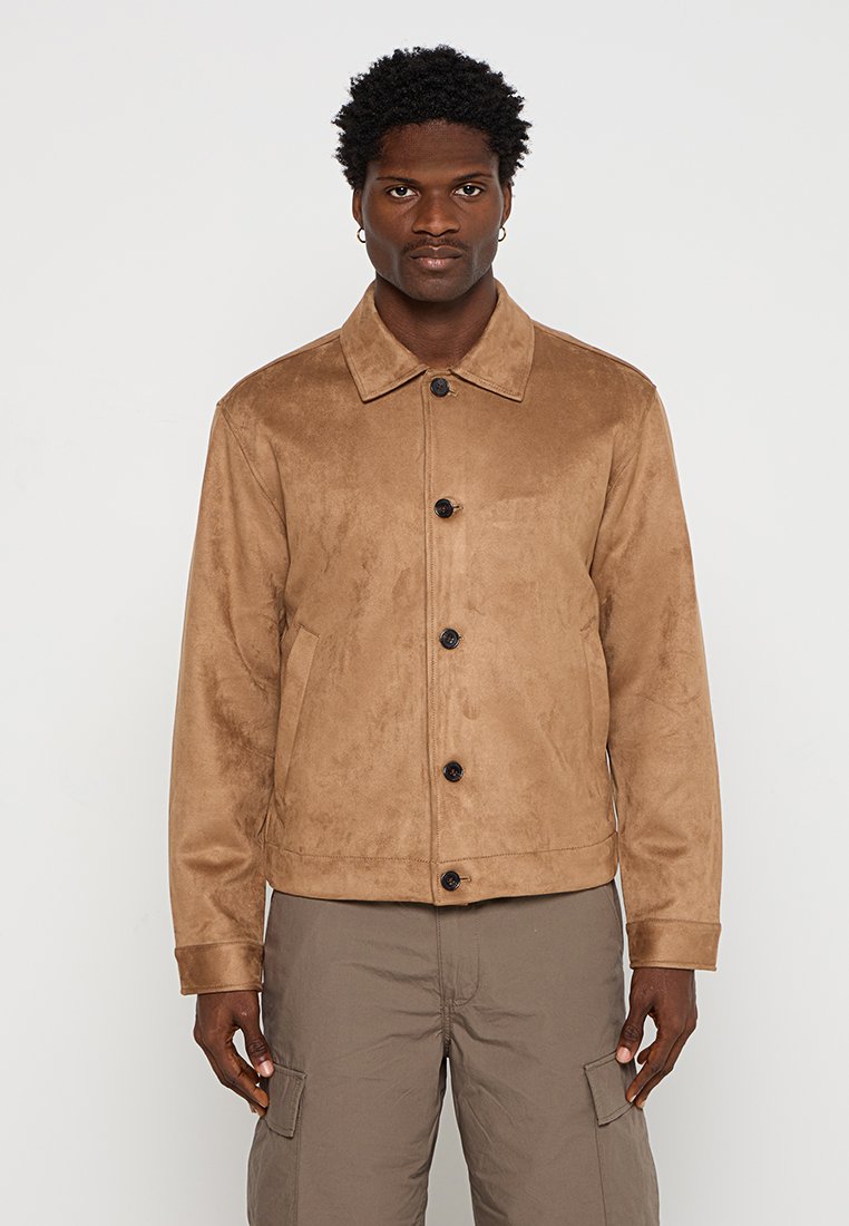 Braune Wildlederjacke mit klassischem Kragen, vorderen Knöpfen und seitlichen Taschen. Glatte Textur und taillierte Passform, kombiniert mit Cargo-Hosen.