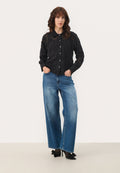 Schwarzes, blumenmusterndes Hemd mit Knöpfen und Kragen, kombiniert mit weiten, hellblauen Denim-Jeans und schwarzen High Heels mit Schleifen.