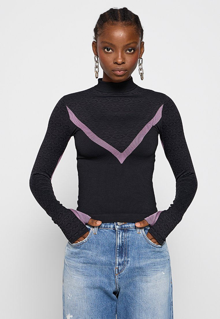 Schwarzes Rollkragenshirt mit gemusterter Textur, lila Chevron-Details und enganliegenden langen Ärmeln. Kombiniert mit blauen hochgeschnittenen Jeans.
