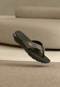 Schwarze und graue Skechers Zehensteg-Sandale mit strukturierter Sohle, die über einem beigen Teppich vor einem beigen Sofa schwebt.