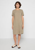 Beige Kleid bis zum Knie mit kurzen Ärmeln und schwarzen Tupfen; runder Ausschnitt; lockere Passform; kombiniert mit hellen, lässigen Sandalen.