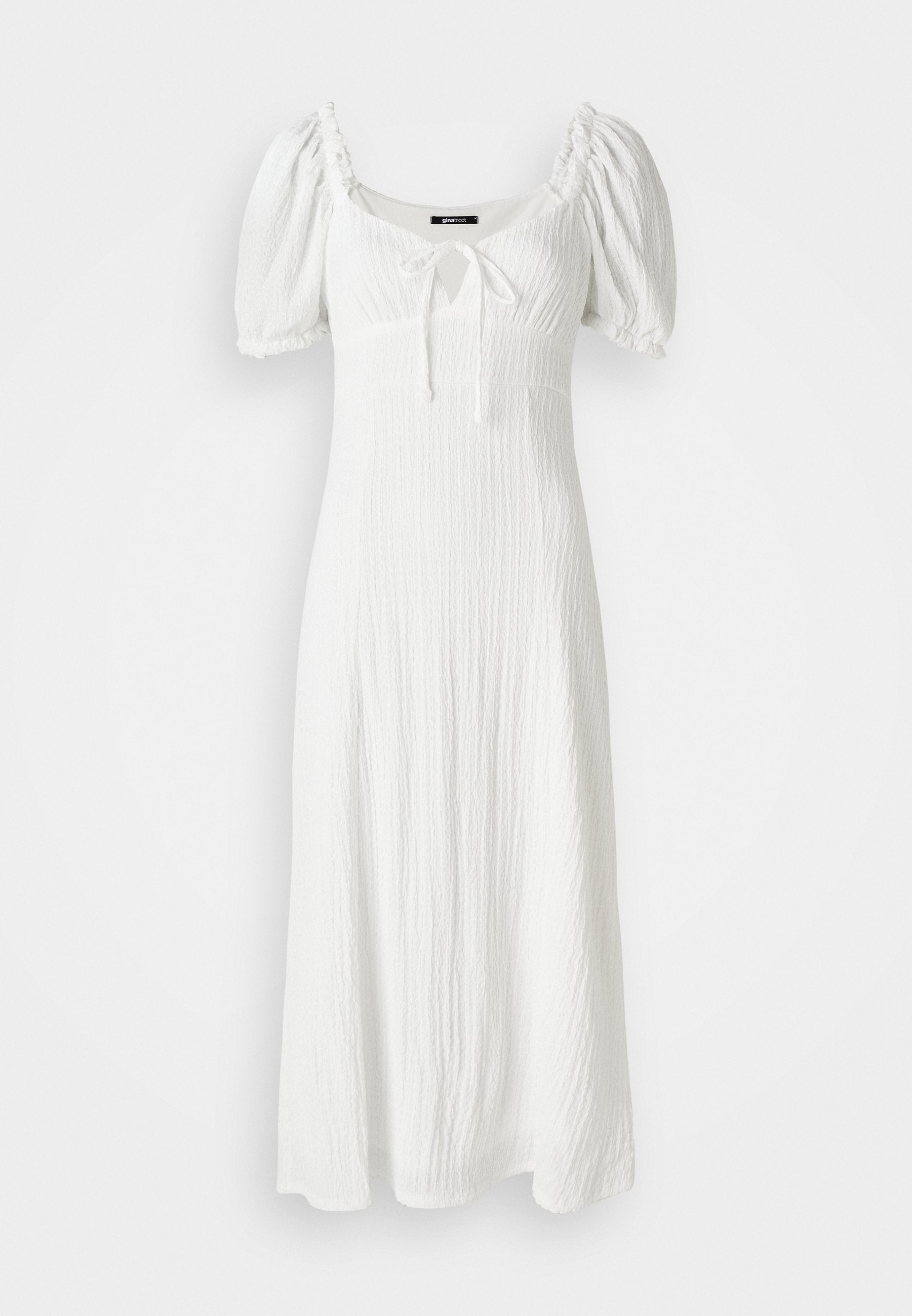 Weißes Kleid aus strukturiertem Stoff, mit Puffärmeln, quadratischem Ausschnitt und einer vorderen Bindegarnitur an der Brust. Fällt bis zur Mitte der Wade.