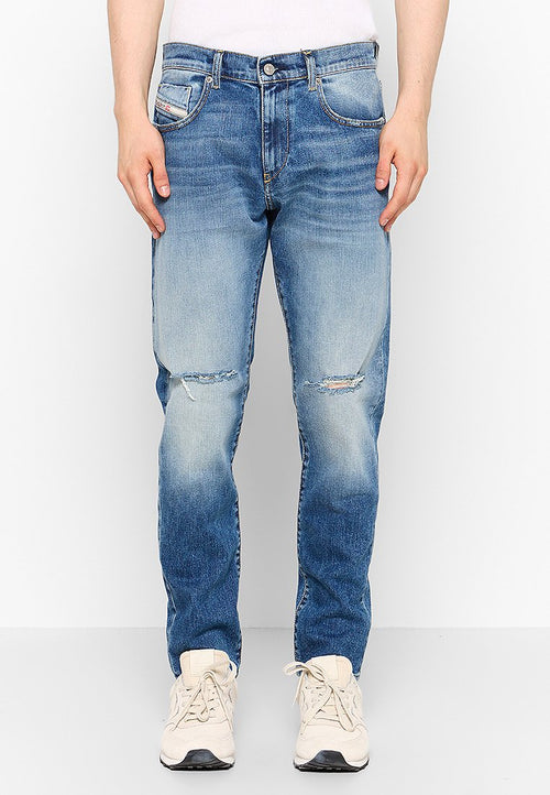 Verblasste blaue Jeans im Slim-Fit-Stil, mit ausgefransten Kniedetails, fünf Taschen und einem Knopfverschluss. Getragen mit hellen Sneakers.