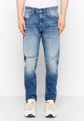 Verblasste blaue Jeans im Slim-Fit-Stil, mit ausgefransten Kniedetails, fünf Taschen und einem Knopfverschluss. Getragen mit hellen Sneakers.