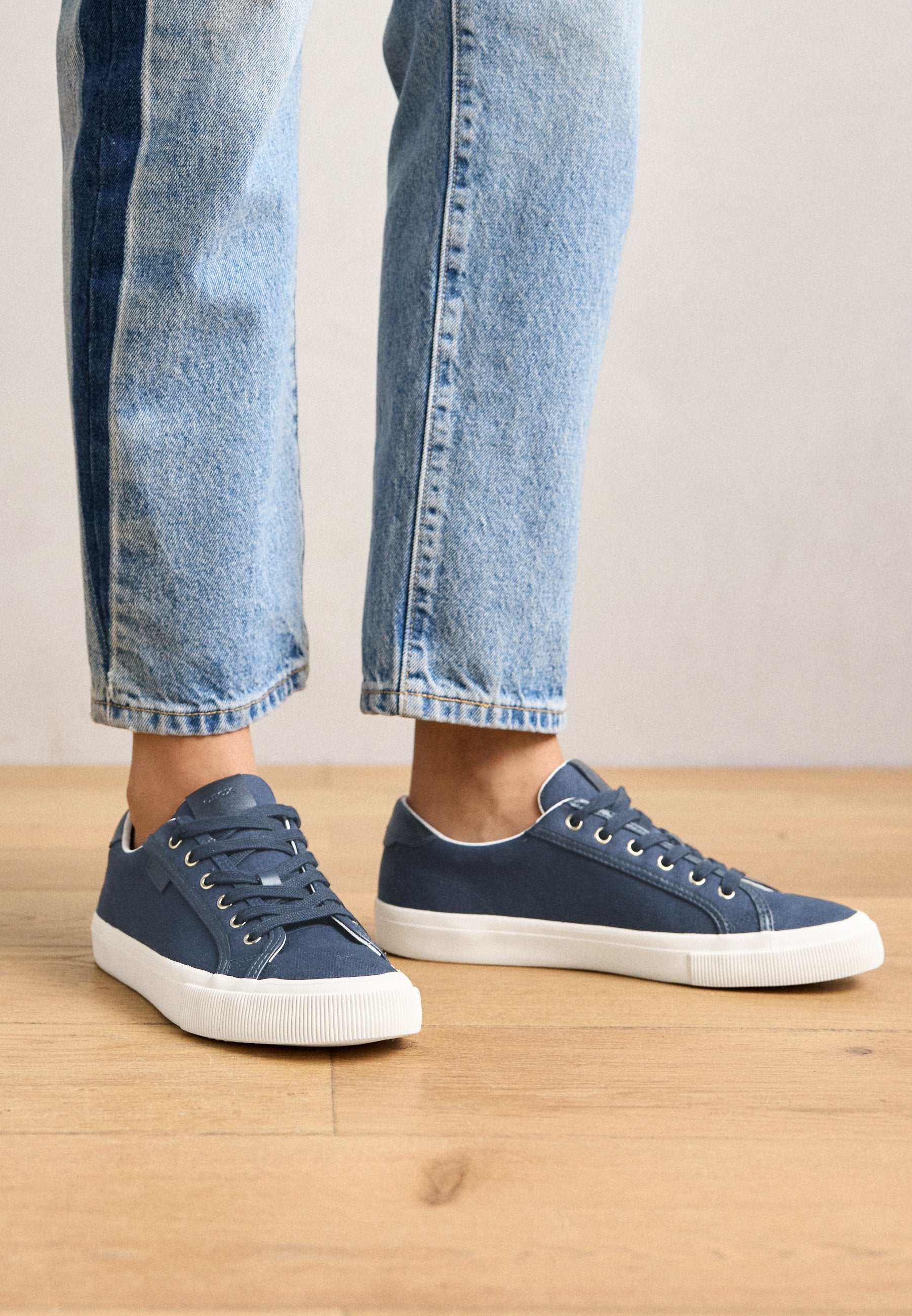 Blaue Canvas-Sneaker mit einer weißen Gummisohle, ausgestattet mit runden Schnürsenkeln und Metallösen. Das Design ist niedrig geschnitten mit einer eleganten Silhouette.