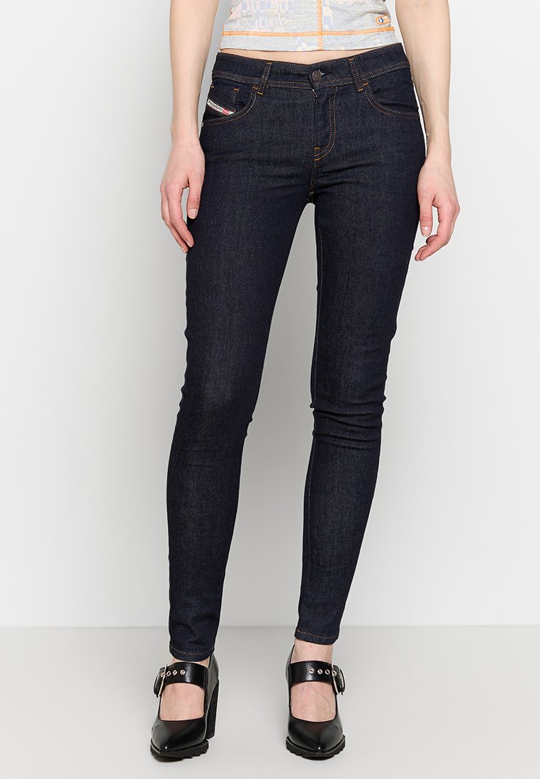 Dunkelblaue Skinny Jeans mit mittelhohem Bund, Kontrastnähten, fünf Taschen und einem Knopfverschluss. Tragen Sie sie mit schwarzen High Heels.