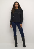 Schwarzes Strickoberteil mit strukturiertem Rautenmuster, Ballonärmeln und rundem Ausschnitt, kombiniert mit dunkelblauen Skinny Jeans und kniehohen schwarzen Stiefeln.