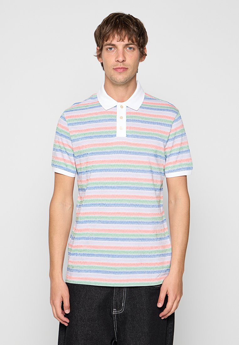 Junger Mann trägt ein kurzärmliges Poloshirt mit pastellfarbenen horizontalen Streifen in Weiß, Pink, Grün und Blau, kombiniert mit schwarzen Hosen.