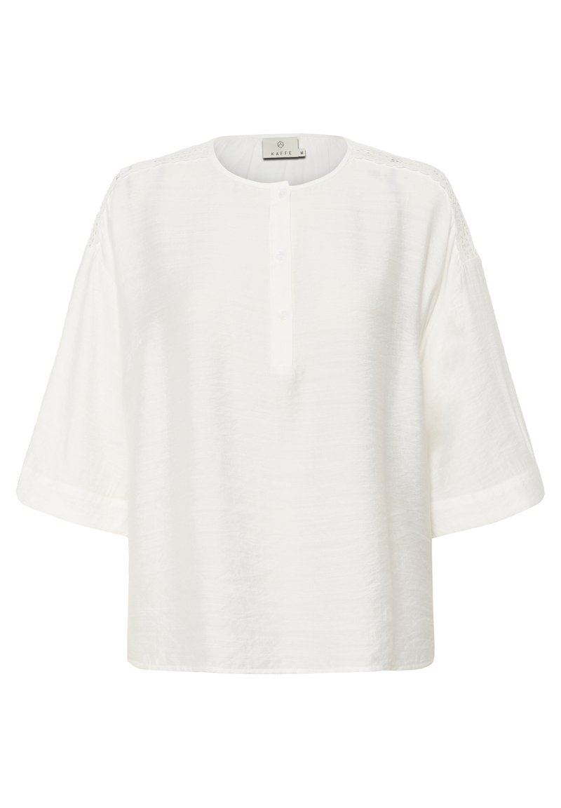 Weiße Bluse mit rundem Halsauschnitt, Knopfleiste mit fünf Knöpfen und kurzen Ärmeln. Verfügt über strukturiertes Material und Spitzenelemente an den Schulternähten.