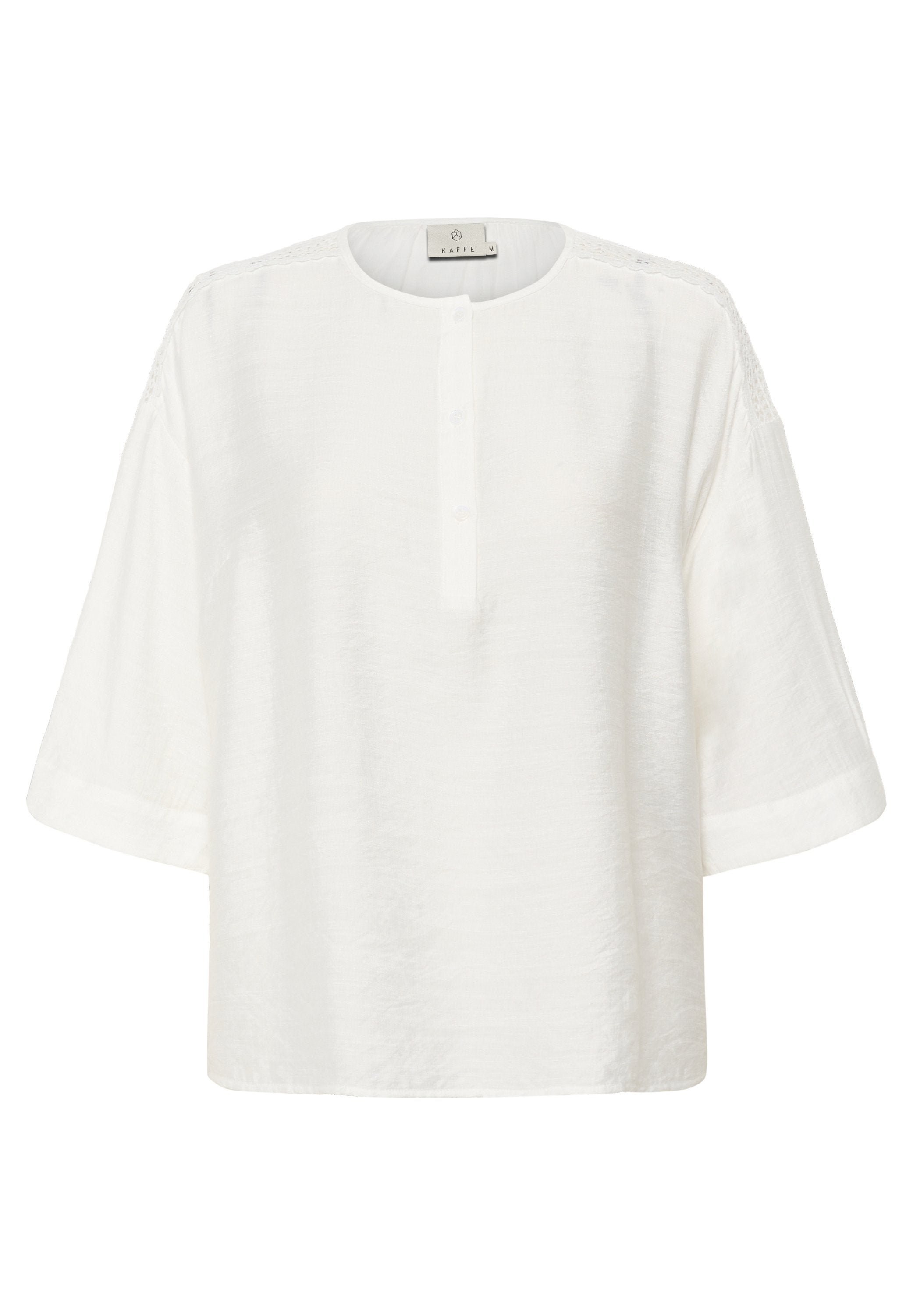 Weiße Bluse mit rundem Halsauschnitt, Knopfleiste mit fünf Knöpfen und kurzen Ärmeln. Verfügt über strukturiertes Material und Spitzenelemente an den Schulternähten.