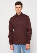 Bordeauxfarbenes Langarmhemd mit Button-Down-Kragen, Brusttasche und vorderen Knopfverschlüssen. Glattes Material und taillierte Passform, getragen mit Jeans.