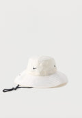 Weißer breitkrempiger Bucket Hat mit schwarzem Nike-Swoosh-Logo und verstellbarem schwarzem Kinnriemen auf einfachem Hintergrund.