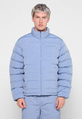 Helle blaue Puffjacke mit hohem Kragen, Reißverschluss und horizontalen Nähten. Verfügt über ein Logo auf der linken Seite und seitliche Taschen.