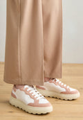 Weiße Sneaker mit rosa Wildleder-Akzenten, runder Zehenform, dicker cremefarbener Sohle und Schnürdesign. Getragen mit beigen, weit geschnittenen Hosen.