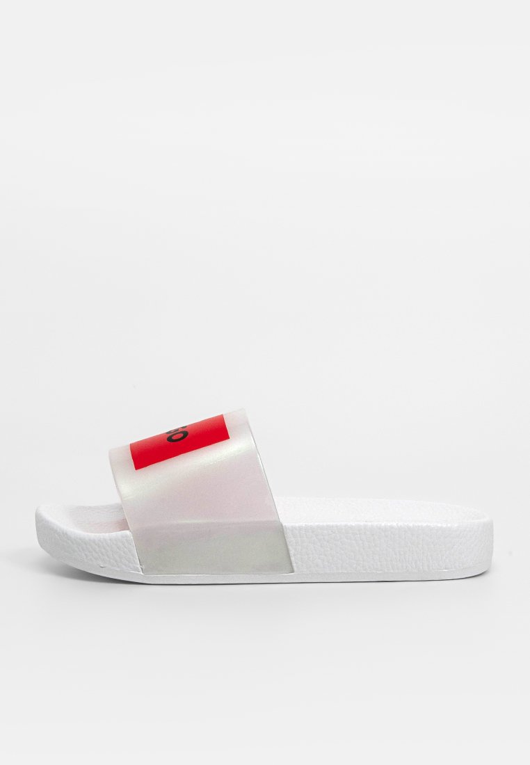 Transparente Kunststoff-Sandale mit breitem Riemen, der einen roten Akzent und schwarzes Logo besitzt; strukturierte weiße Sohle; minimalistisches Design.