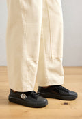 Schwarze Ledersneaker mit strukturierter Oberfläche, runder Form, Schnürdesign und einem markanten weißen Logoakzent an der Seite.