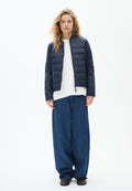 Marineblauer, gesteppter Pufferjacke mit Stehkragen, kombiniert mit einem weißen Hemd und lockeren, weit geschnittenen blauen Jeans. Strukturierten Stoffakzenten.