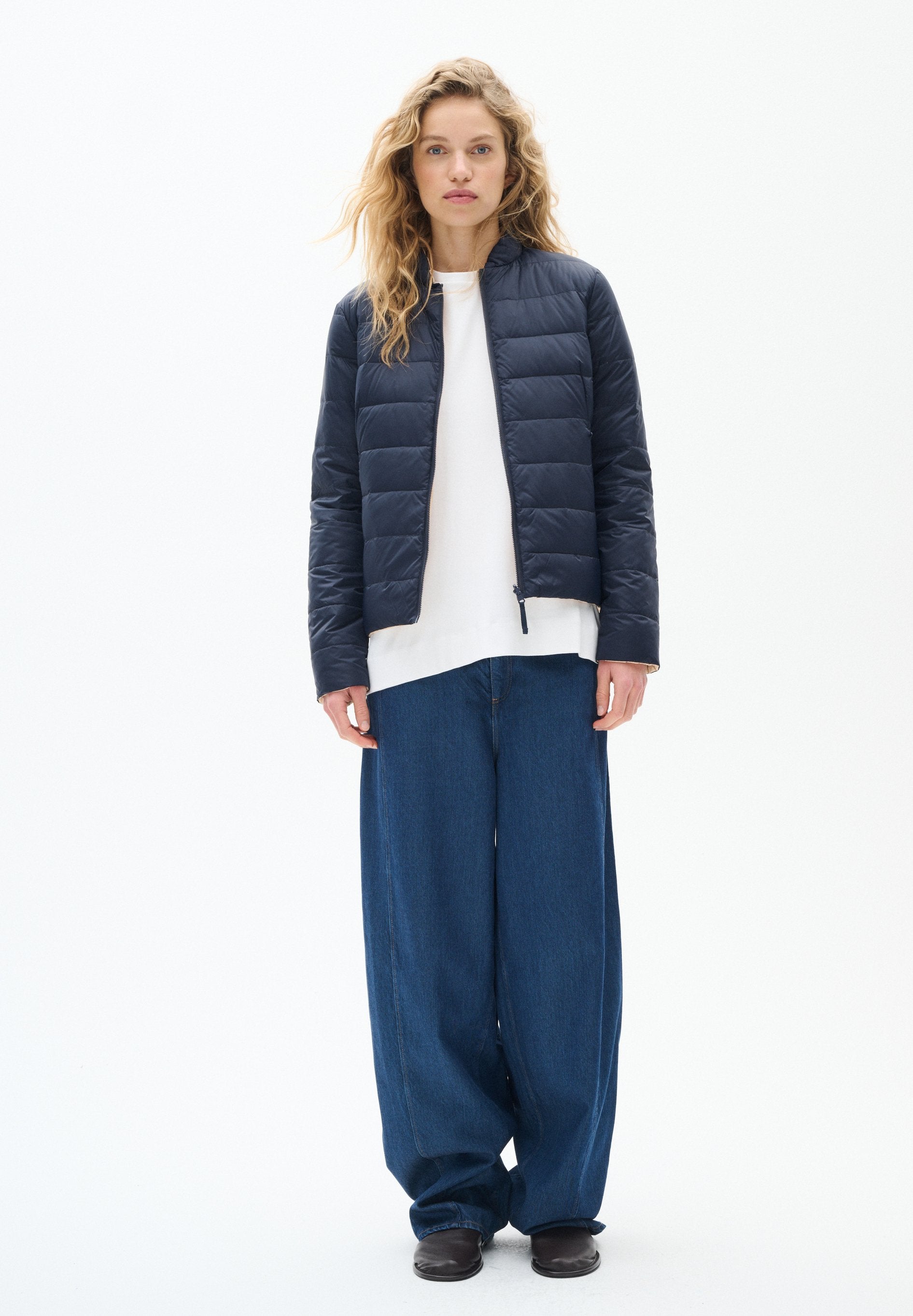 Marineblauer, gesteppter Pufferjacke mit Stehkragen, kombiniert mit einem weißen Hemd und lockeren, weit geschnittenen blauen Jeans. Strukturierten Stoffakzenten.
