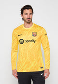 Mann trägt gelbes, gemustertes Langarmtrikot von FC Barcelona mit Spotify-Logo, steht vor einfachem Hintergrund.