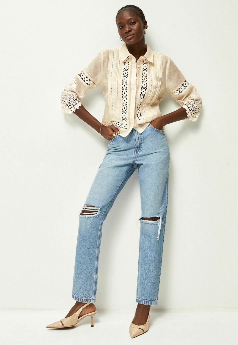 Leinen-Hemd mit Knopfleiste und aufwendigen Spitzenverzierungen, hellbeige Farbe, kombiniert mit hoch taillierten, verwaschenen blauen Jeans und nudefarbenen Slingback-Pumps.