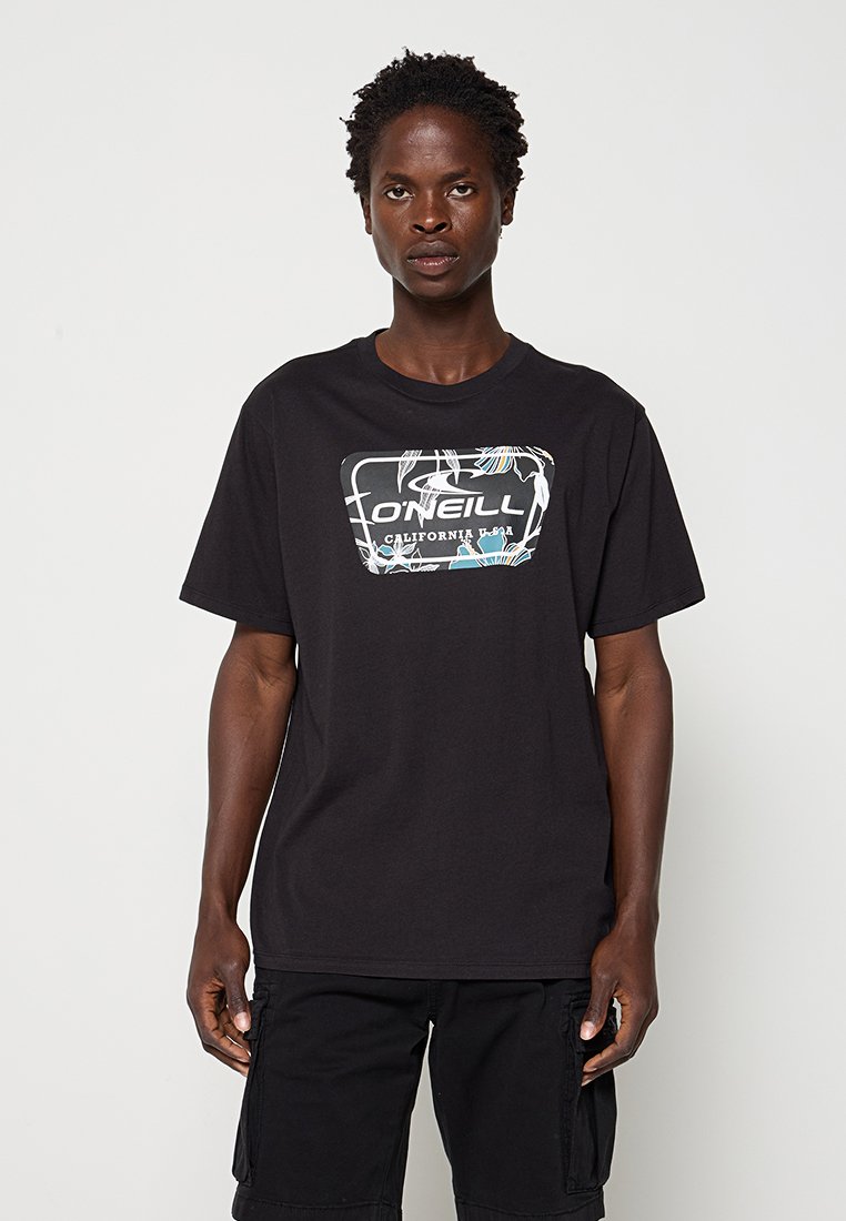 Mann trägt ein schwarzes O'Neill T-Shirt mit floralem Logo und schwarze Cargo-Shorts, steht vor einem schlichten hellgrauen Hintergrund.