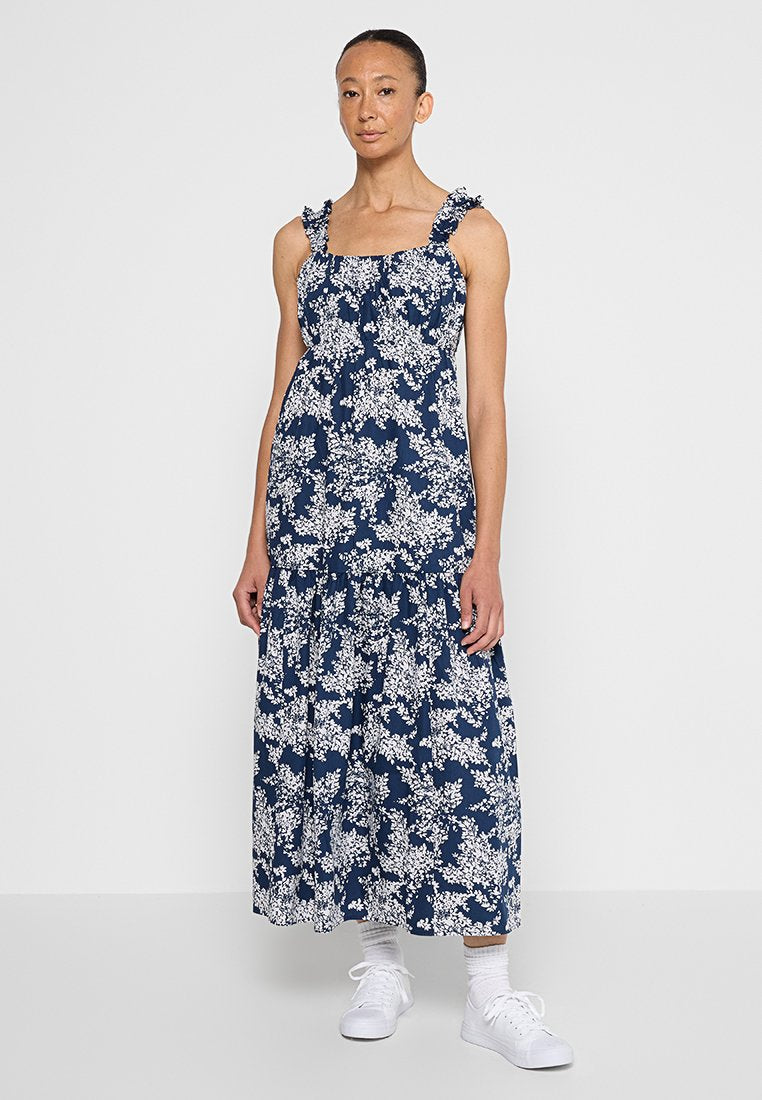 Navyblaues Maxikleid mit floralem Muster, Rüschenträgern und fließender Silhouette, versehen mit weißen Blumenmustern und kombiniert mit weißen Sneakern.