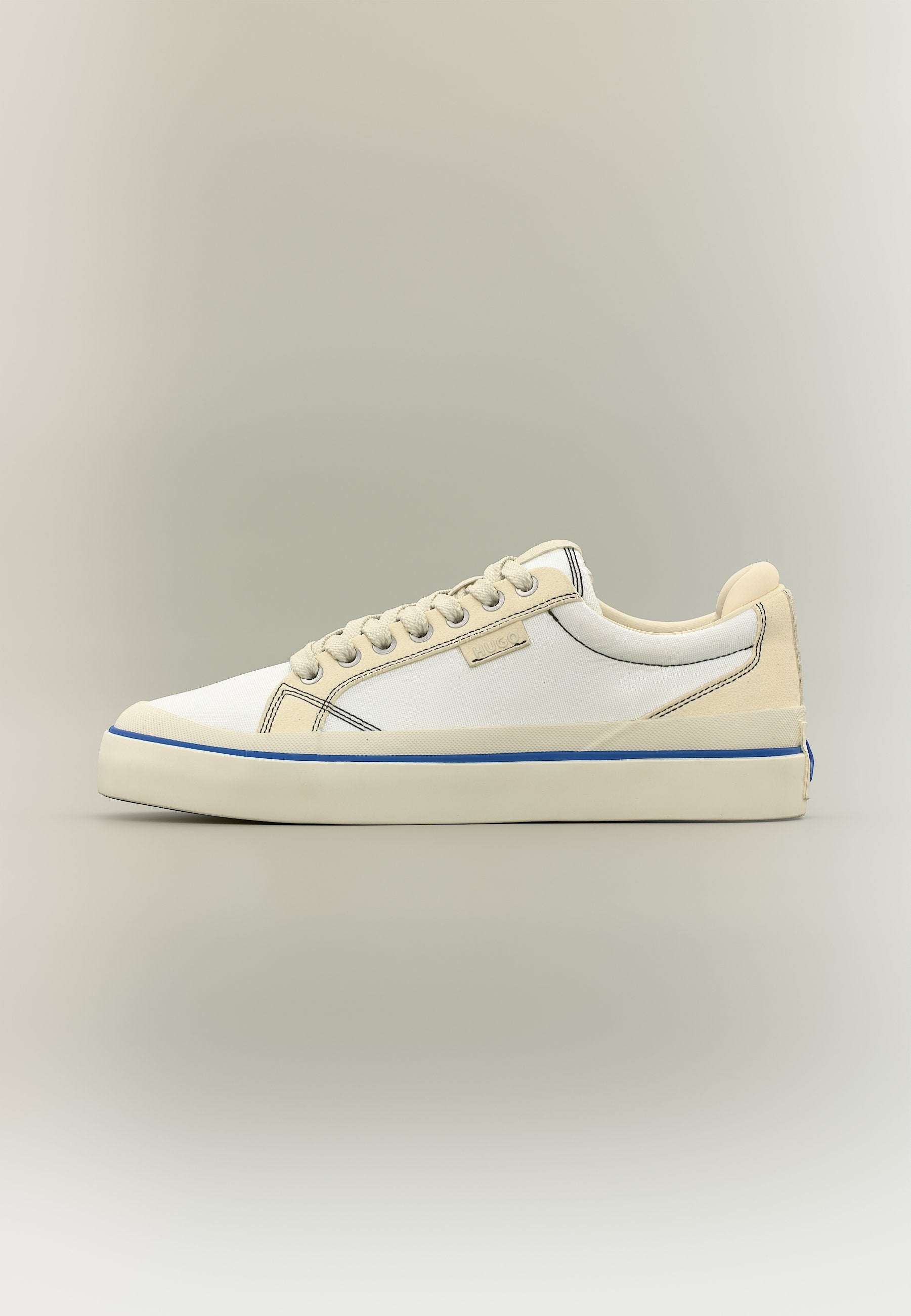 Beiger und weißer Sneaker in niedriger Ausführung mit Schnürverschluss vorne, blauer Streifen an der Sohle und dezentem Markenetikett an der Seite.