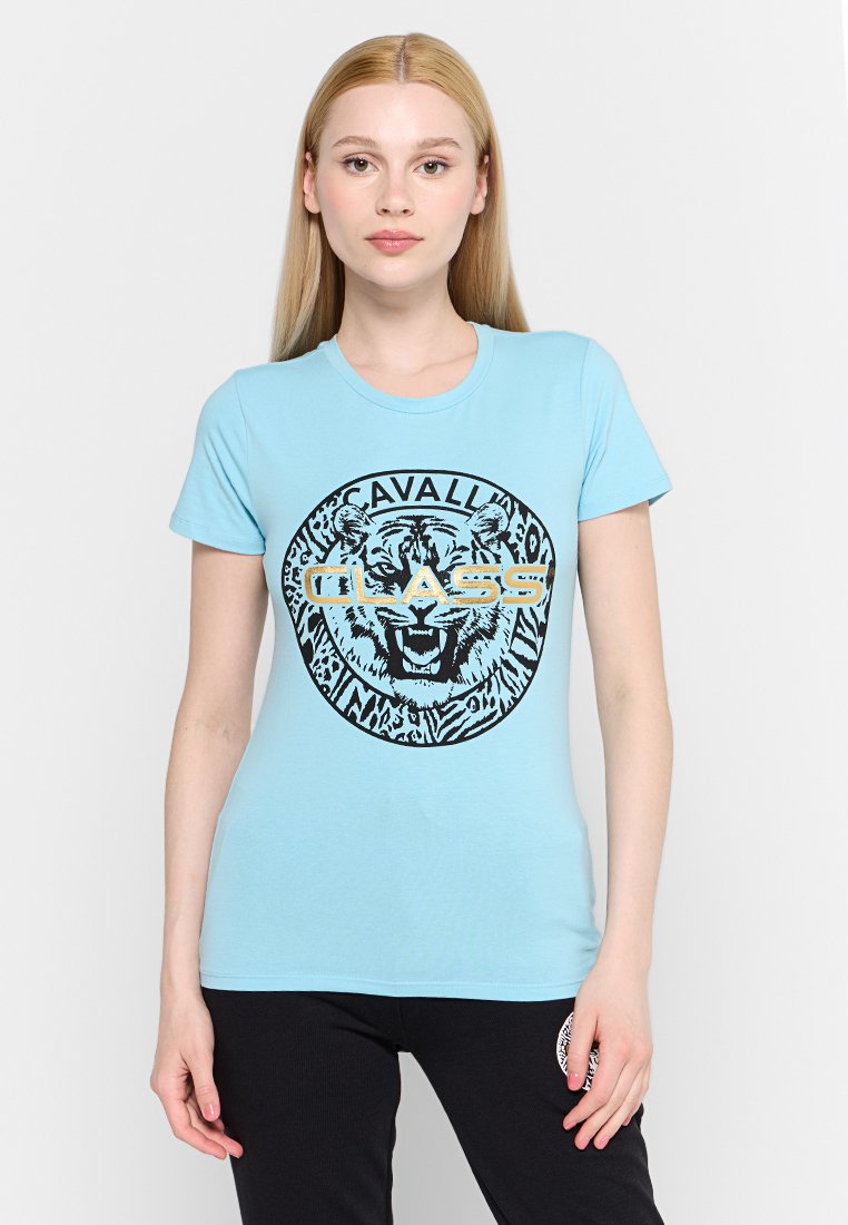 Helle blaue T-Shirt mit einem runden schwarzen und goldenen Grafik, die einen Löwenkopf und den Text "CAVALLI CLASS" zeigt. Kurze Ärmel, Rundhalsausschnitt.