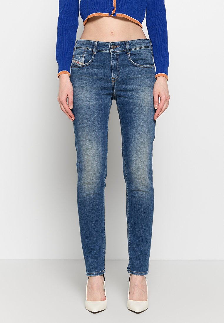 Dünne blaue Jeans aus Denim mit verwaschenem Aussehen, fünf Taschen und einem Reißverschluss. Kombiniert mit cremefarbenen High Heels.