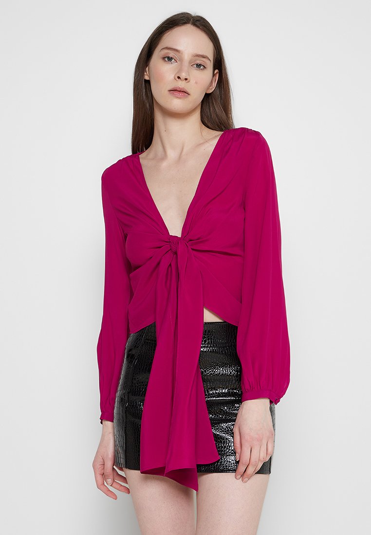 Fuchsia Bluse mit langen Ärmeln, tiefem V-Ausschnitt und Frontknoten detail. Strukturierter schwarzer Minirock mit glänzender Oberfläche. Glattes Material.