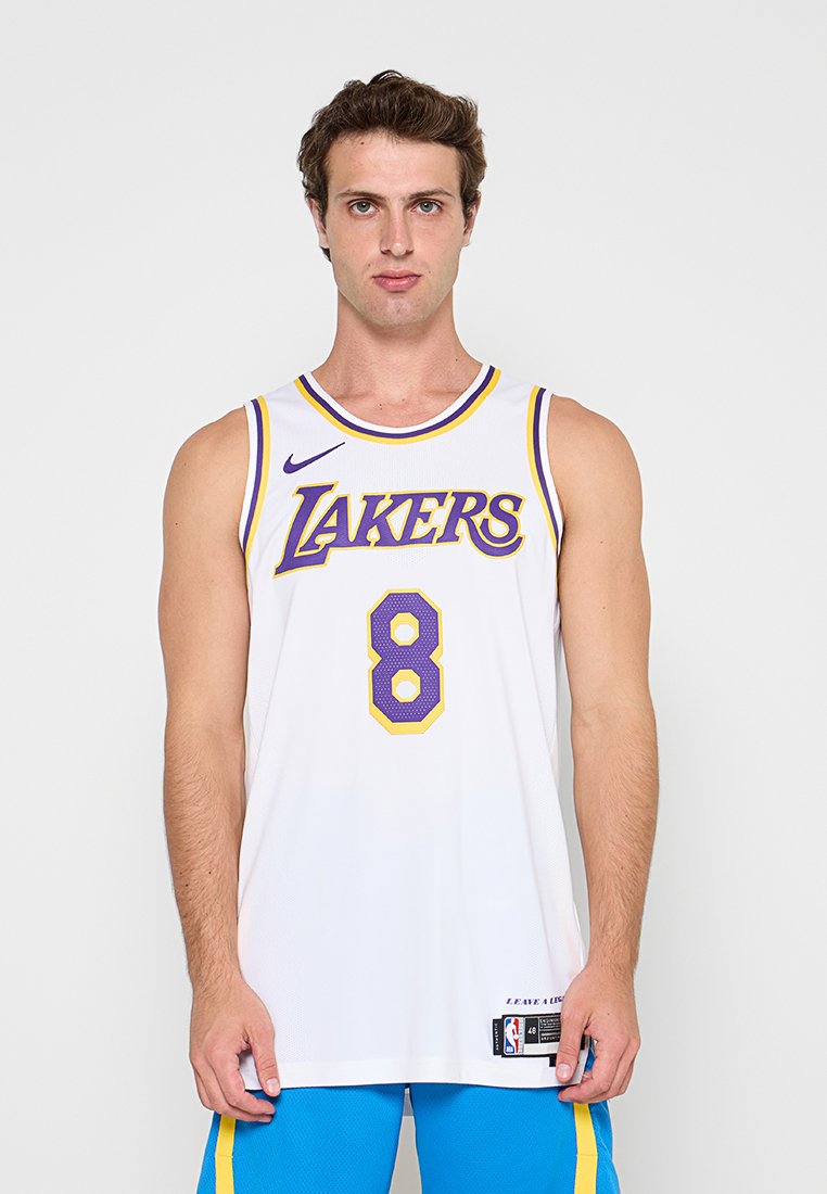 Mann trägt ein weißes Lakers Basketballtrikot mit der Nummer 8 und blaue Shorts und steht vor einem schlichten Hintergrund.