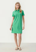 Grünes Polo-Kleid mit kurzen Ärmeln, Knopfleiste und geradem Saum. Glattes, leichtes Material. Getragen mit hellen Sandalen.