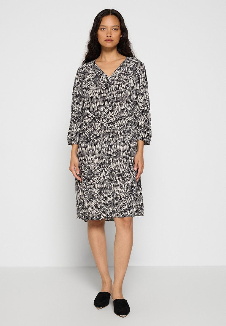Schwarz-creamfarbenes gemustertes Kleid mit langen Ärmeln, V-Ausschnitt und lockerem Schnitt, aus weichem Stoff gefertigt. Kombiniert mit schwarzen Slippern.