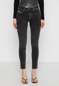 Schwarze Skinny-Jeans mit einer abgedunkelten Textur, ausgestattet mit fünf Taschen und gelben Nähten. Kombiniert mit einem eng anliegenden schwarzen Oberteil und minimalistischen Sandalen.