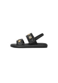 Schwarze flache Sandale mit zwei gepolsterten Riemen, goldfarbenen Knopfdetails und Fersenriemen auf weißem Hintergrund.