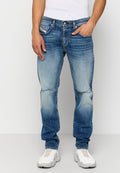 Mann trägt ausgebleichte blaue Jeans mit leichten Abnutzungserscheinungen an den Knien, weiße Slip-On Sneakers und ein weißes ärmelloses Shirt.