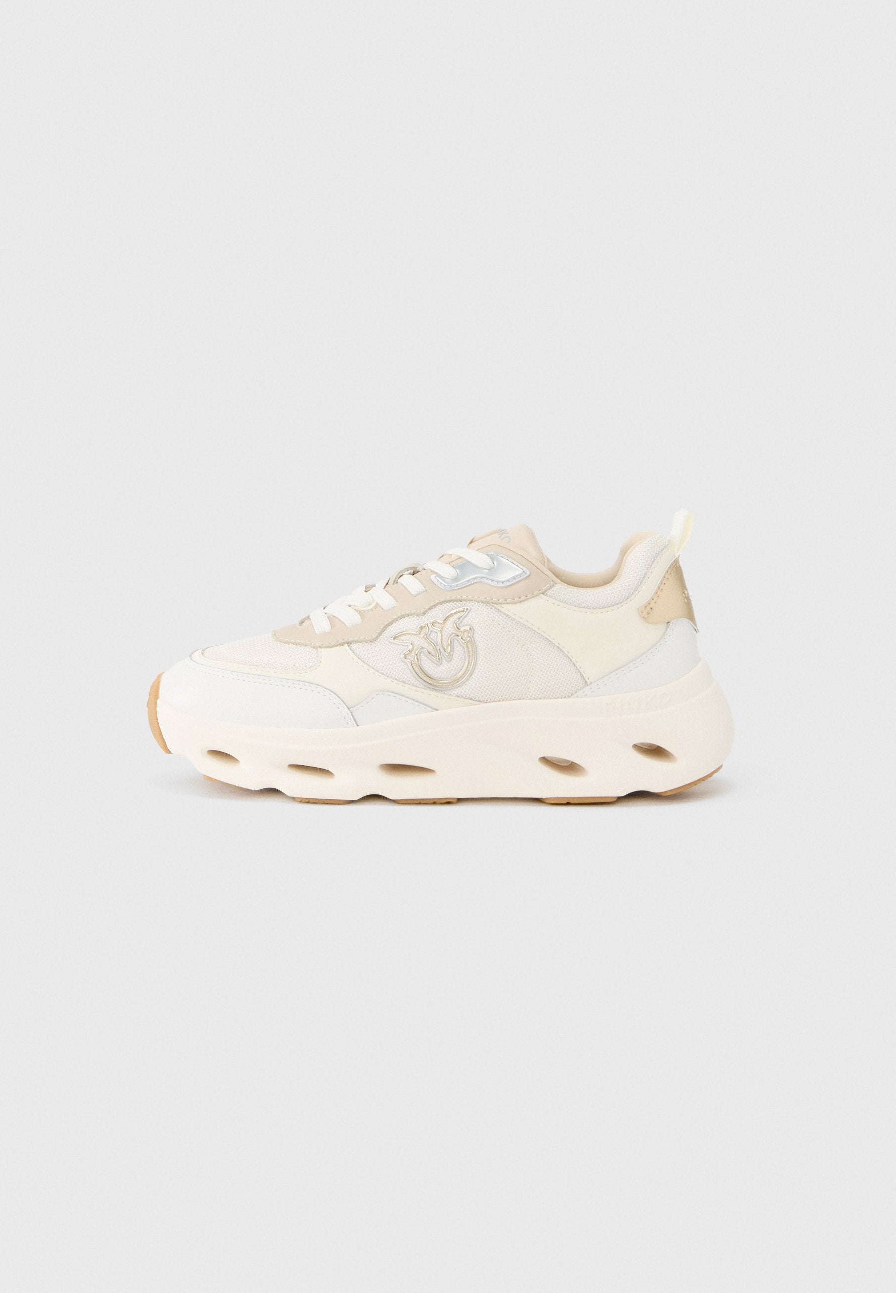 Cremefarbener und beiger Sneaker mit Mesh- und Lederpaneelen, rundem Zehenbereich, weißen Schnürsenkeln, Branding an der Seite und klobiger Sohle mit Aussparungen.