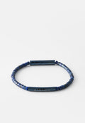 Blaues Perlenarmband mit zylindrischem Verschluss und zentraler Metallstange, auf der "AIGNER" eingraviert ist, vor weißem Hintergrund.