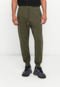 Olivgrüne Sweatpants mit elastischem Bund, verstellbarem Kordelzug und seitlichen Streifen. Kombiniert mit schwarzen Sportschuhen.