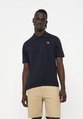 Mann trägt ein schwarzes kurzärmliges Polo mit kleinem Zebra-Logo und beigefarbenen knielangen Shorts, steht vor einem weißen Hintergrund.