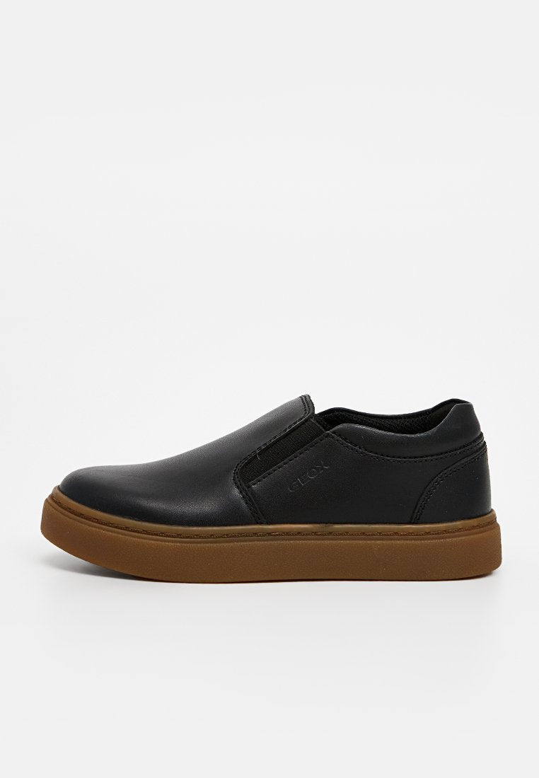 Schwarzer Slipper aus glattem Lederobermaterial, mit elastischen Seitenpaneelen und einer braunen Gummisohle. Minimalistisches Design ohne sichtbare Verzierungen.