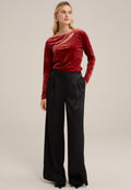 Rotes Samtoberteil mit langen Ärmeln und Cut-Out-Detail, kombiniert mit hochgeschnittenen schwarzen weiten Hosen mit Falten und ausgestellten Säumen.