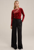 Rotes Samtoberteil mit langen Ärmeln und Cut-Out-Detail, kombiniert mit hochgeschnittenen schwarzen weiten Hosen mit Falten und ausgestellten Säumen.