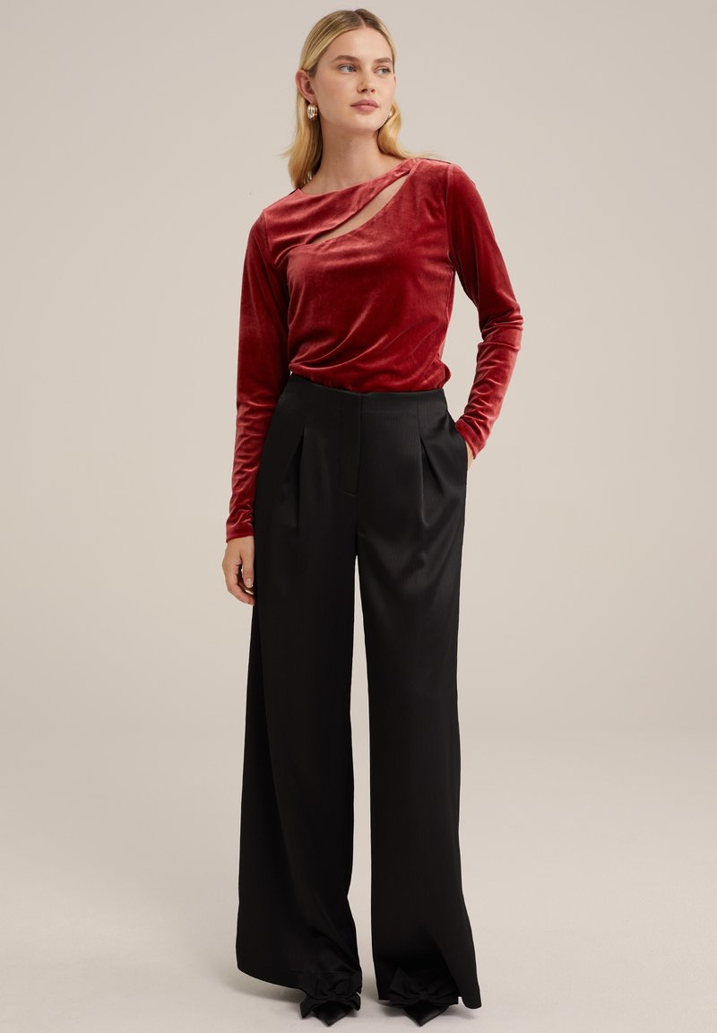 Rotes Samtoberteil mit langen Ärmeln und Cut-Out-Detail, kombiniert mit hochgeschnittenen schwarzen weiten Hosen mit Falten und ausgestellten Säumen.