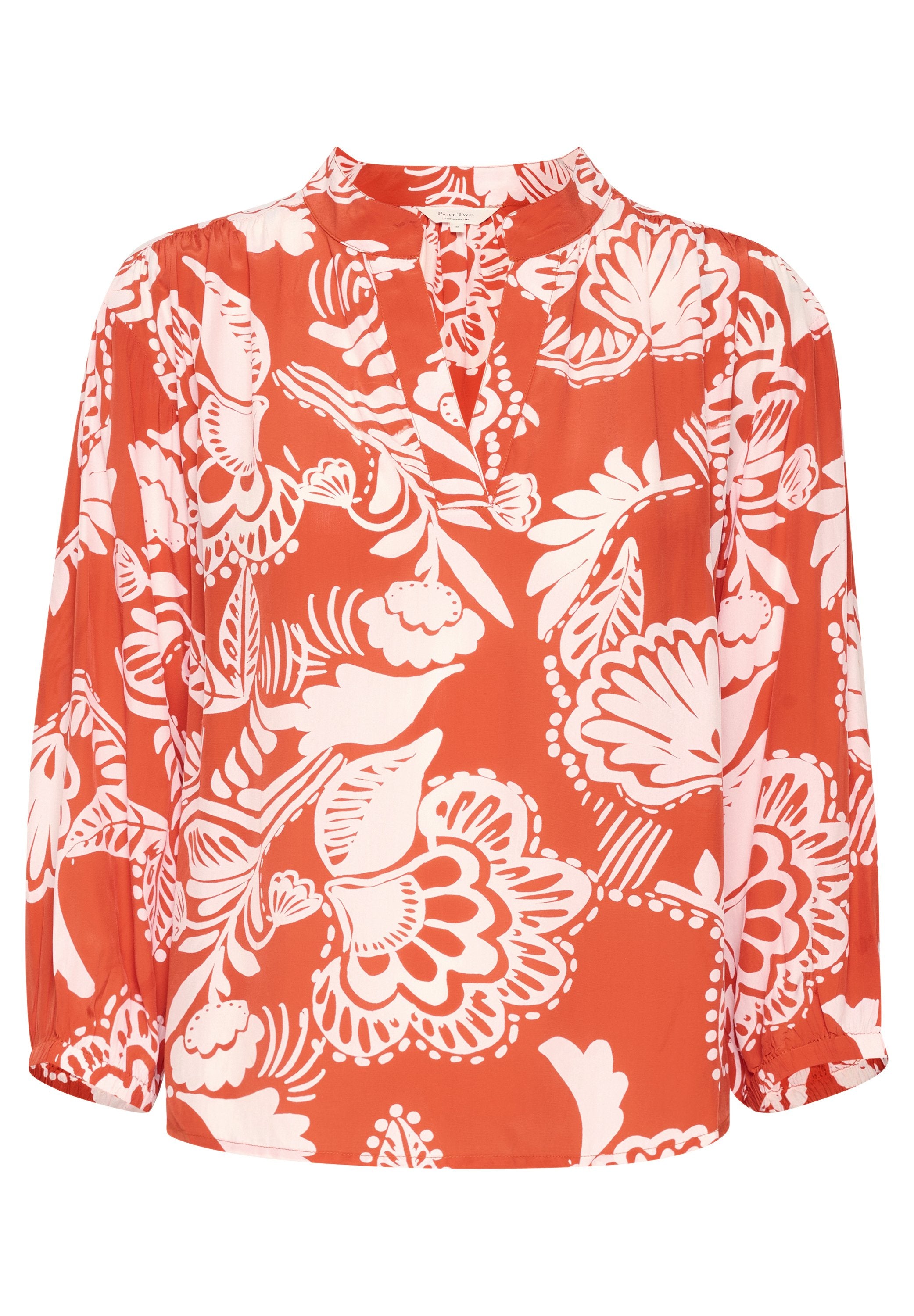 Rote Bluse mit langen Ärmeln, die weiße Blumenmuster aufweist, einen V-Ausschnitt hat und geraffte Details an den Ärmeln besitzt. Glatte Stofftextur.