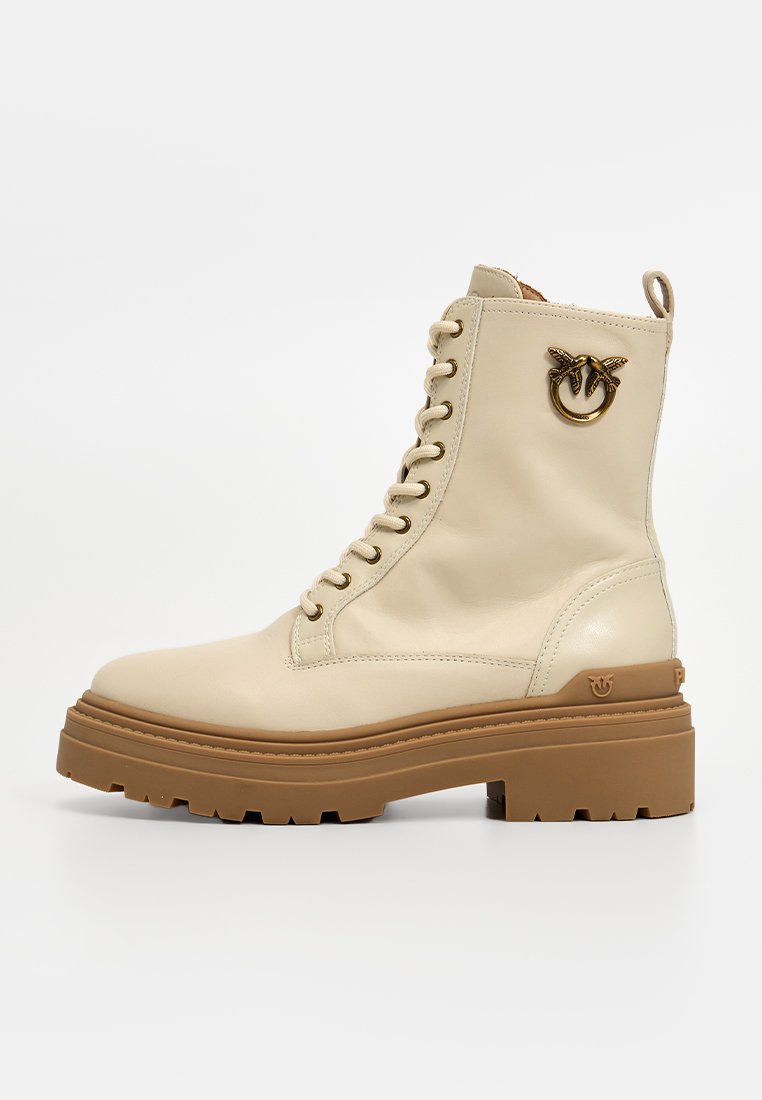 Beige Leder Stiefeletten mit einer klobigen braunen Sohle, Schnürdesign und dekorativem goldenen Logo an der Seite.