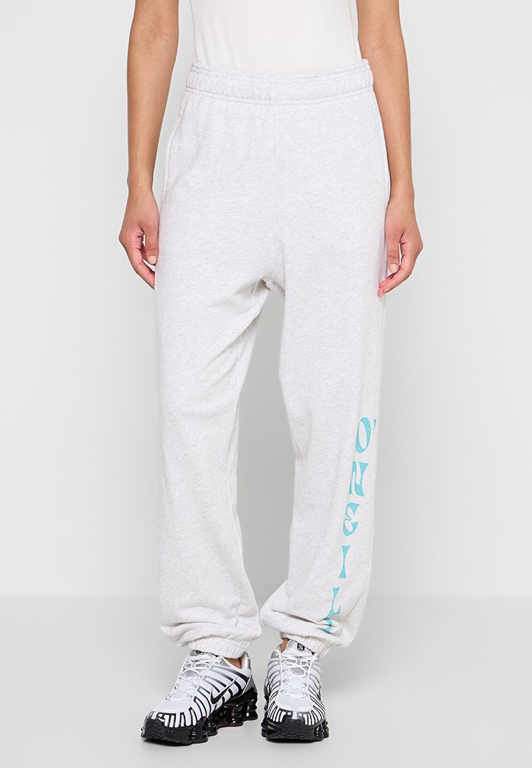 Graue Freizeit-Hosen mit lockerem Schnitt, elastischem Bund und türkisfarbenem Branding entlang des linken Beins. Hergestellt aus weichem Baumwollmischgewebe.