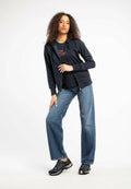 marinefarbener Zip-Hoodie, schwarzes T-Shirt mit rotem Text darunter, lockere blaue Jeans und schwarze Sneakers mit grauen Akzenten. Glattes Material und bequeme Passform.